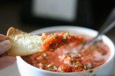 a hand holding a piece of bread over a bowl of salsa