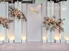 three floral arrangements are on display in front of a white backdrop with gold lettering and candles