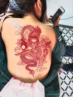 a woman with a dragon tattoo on her back and holding a cell phone in her hand