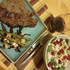 there is a plate with meat, asparagus and strawberries next to a bowl of salad