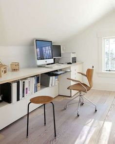 a computer desk with two monitors on top of it next to a chair and bookshelf