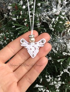 a hand holding an ornament in front of a christmas tree with white flowers