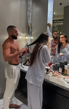 a man and woman standing in front of a bathroom mirror brushing their hair with scissors