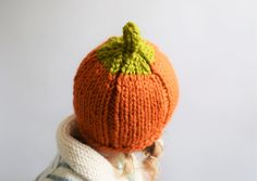 a child wearing an orange knitted hat with a green leaf on the top and bottom