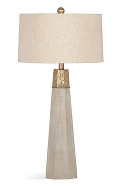 a table lamp with a white shade on it and a gold metal frame around the base