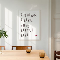 a dining room table with two chairs and a plant on the wall next to it that says i think i like this little life