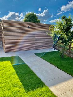 a backyard with green grass and a wooden fence on the other side, water spewing from a hose