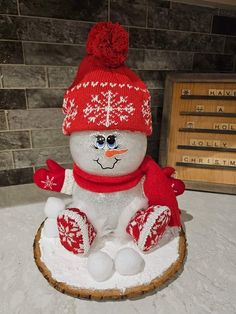 a snowman sitting on top of a tree stump wearing a red hat and scarf