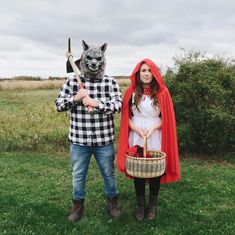 two people dressed up in costumes standing on grass with one holding a basket and the other wearing a wolf mask