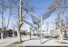 a metal sculpture sitting on the side of a road next to some trees and buildings