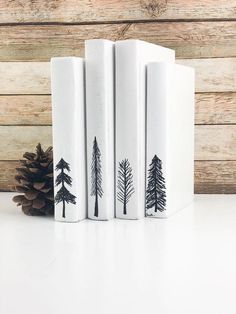 three bookends with trees painted on them next to a pine cone and wood plank wall