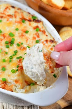 a hand dipping a piece of bread into a casserole with cheese and chives