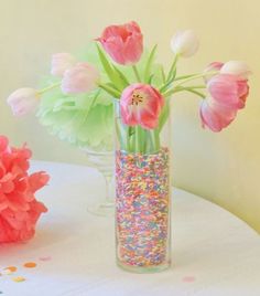 a vase filled with pink flowers sitting on top of a table next to confetti