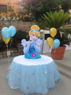 a table topped with balloons and a princess figure sitting on it's top in front of a house