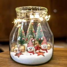 a glass jar filled with snowmen and christmas trees on top of a wooden table