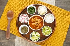 a wooden plate topped with bowls filled with different types of food next to a spoon