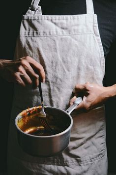 a person in an apron holding a ladle and stirring bowl with food on it