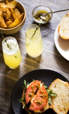 a black plate topped with a cut in half sandwich next to two glasses of juice