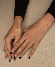 a woman's hands with black nail polish and stars on their fingers, resting on a beige surface