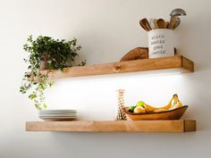 two wooden shelves with plates and bowls on them, one holding bananas and the other serving utensils