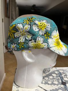 a white mannequin head wearing a blue hat with yellow and white flowers on it