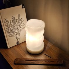 a white vase sitting on top of a wooden table next to a book