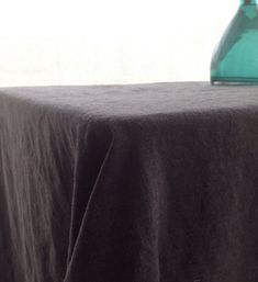 a green vase sitting on top of a table next to a black cloth covered table