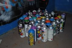 there are many cans of spray paint in front of a wall with graffiti on it