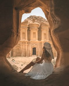 a woman in a white dress and hat sitting on the side of a rock formation