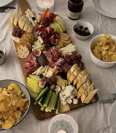 a wooden platter filled with cheese, crackers and other snacks on top of a white table cloth