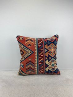 an orange and blue decorative pillow on a white carpet with a wall in the background