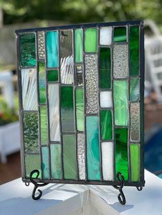 a green and white stained glass panel on a stand next to a swimming pool with chairs in the background