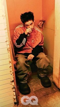 a young man sitting on top of a wooden bench in a bathroom next to a door