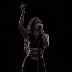 a woman with her arms up in the air while holding a microphone and singing on stage