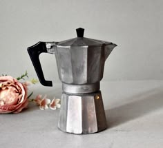 a silver coffee pot sitting next to a pink flower