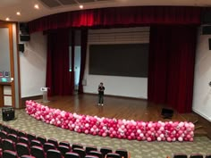 a person standing in front of a stage with red and pink balloons on the floor