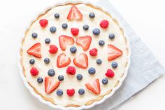 a pie topped with strawberries and blueberries on top of a white tablecloth