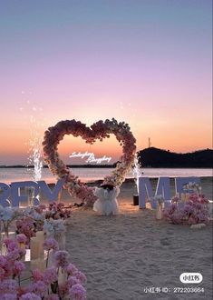 a heart - shaped sign on the beach with flowers and candles in front of it