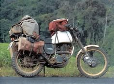 an old motorcycle is parked on the side of the road in front of some trees