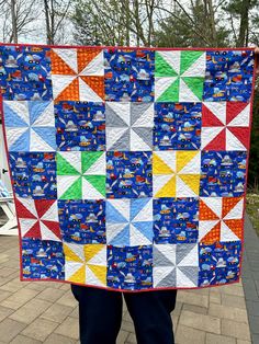 a person holding up a colorful quilt