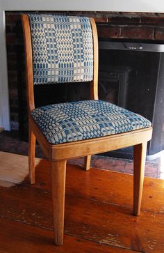 a wooden chair sitting in front of a fire place with a blue patterned seat cover