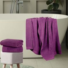 a white bath tub sitting next to a purple towel on top of a wooden stool