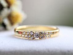 a yellow gold wedding band with five diamonds on the top and bottom, sitting next to a bouquet of flowers