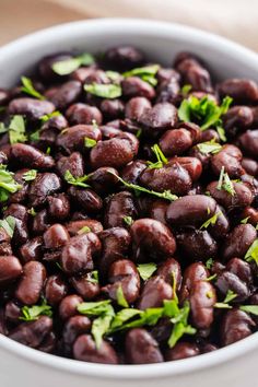 a white bowl filled with black beans and garnished with green leaves on top