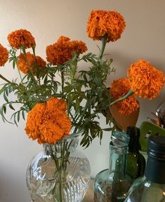 orange flowers are in a clear vase on a table next to other bottles and jars