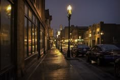 a city street at night with cars parked on the side walk and lights in the windows