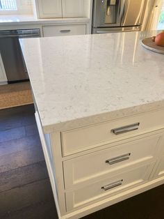 a white kitchen with marble counter tops and stainless steel appliances in the backround