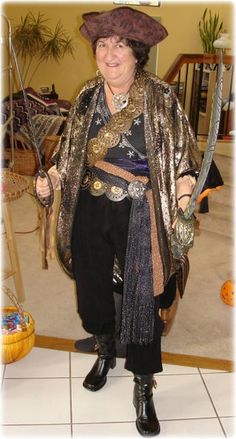 a woman dressed up as a pirate holding two swords and wearing a hat with gold sequins on it