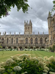 a large building with many windows and lots of flowers in the foreground on a cloudy day