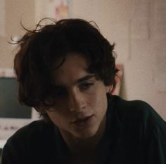 a young man sitting in front of a computer monitor looking at his cell phone while wearing a black shirt